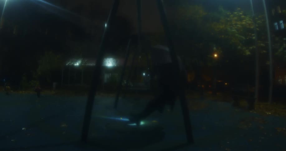 A person swings on a swing set at night and holds a flashlight