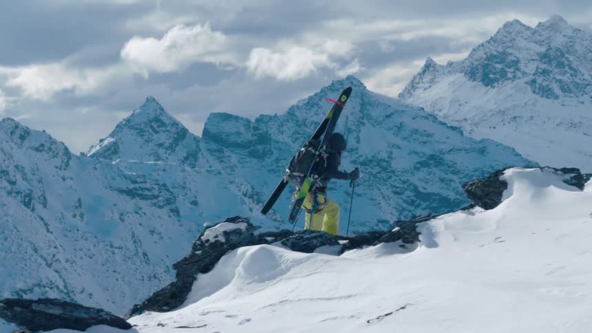 Skier carries skis on his back as he walks using poles on the snowy mountain