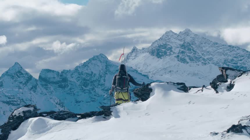 A mountaineer stands atop a mountain while gazing out at the snowy landscape below