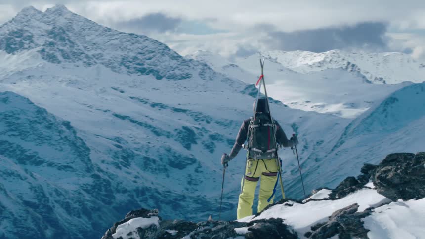 A hiker stands high on a mountain slope and looks out over the snowy valley below