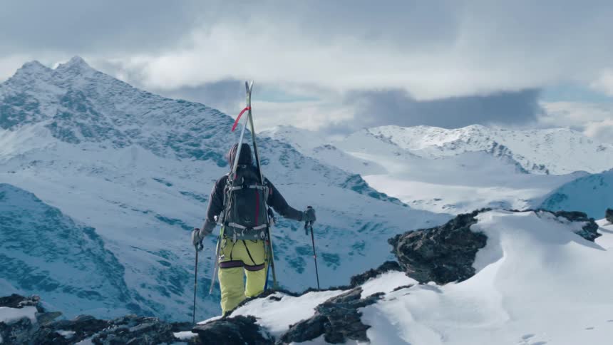 A person stands on the mountain top with skis