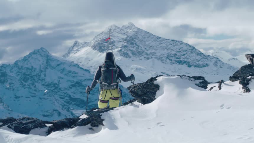 A mountaineer standing atop a mountain ridge looks out at the valley below
