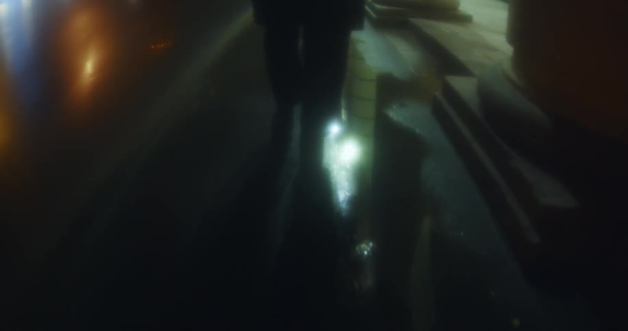 A person following another person down a sidewalk in the rain