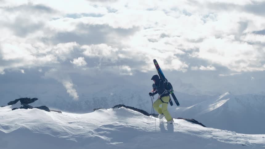 A mountaineer walks across the summit of a mountain ridge with the assistance of trekking poles