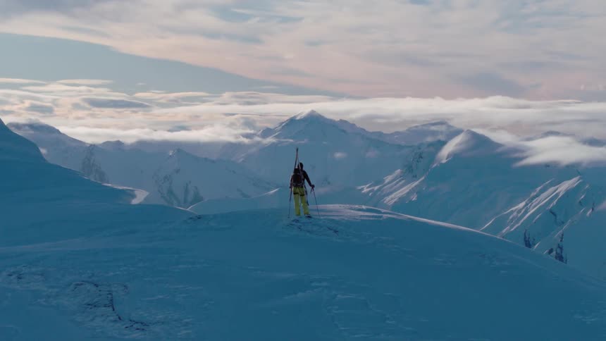 A hiker stands near a snowy cliff to look at the mountain view