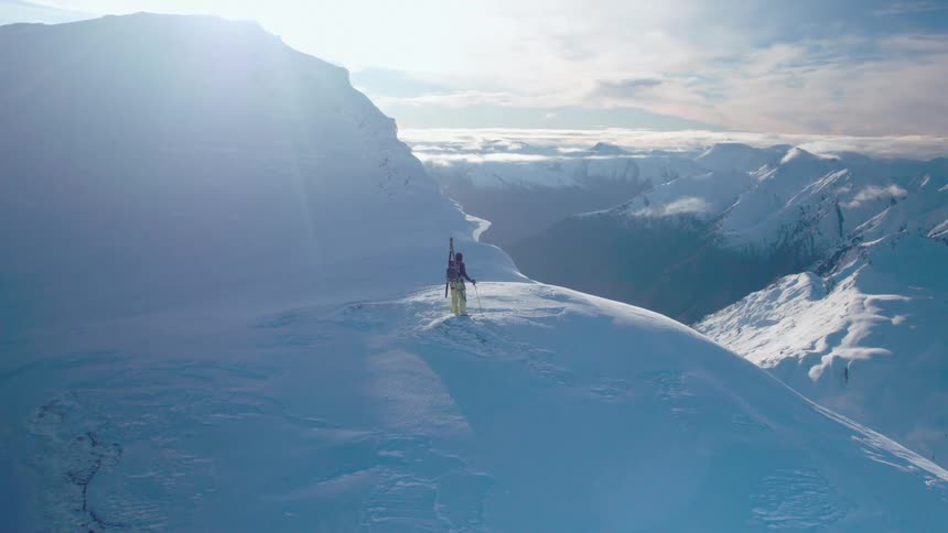A person stands on the mountain top with skis