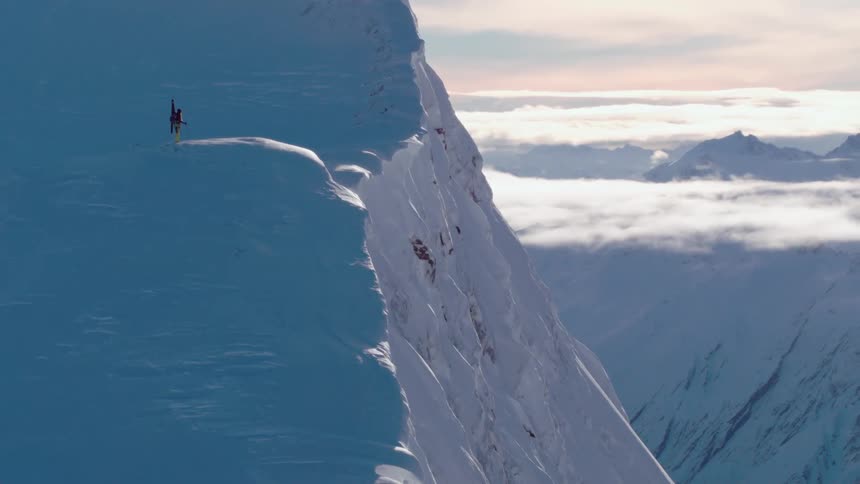 A man standing on the top of a mountain that is covered in snow