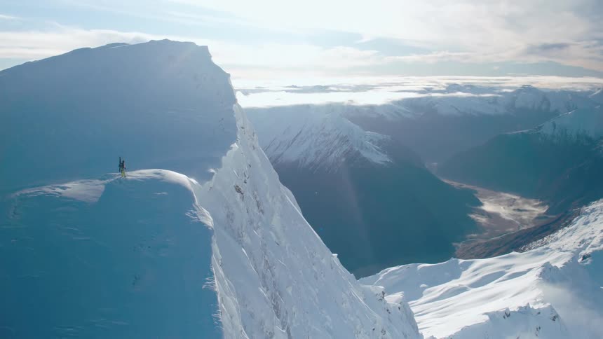 A person is on the cliff of the mountain with skis