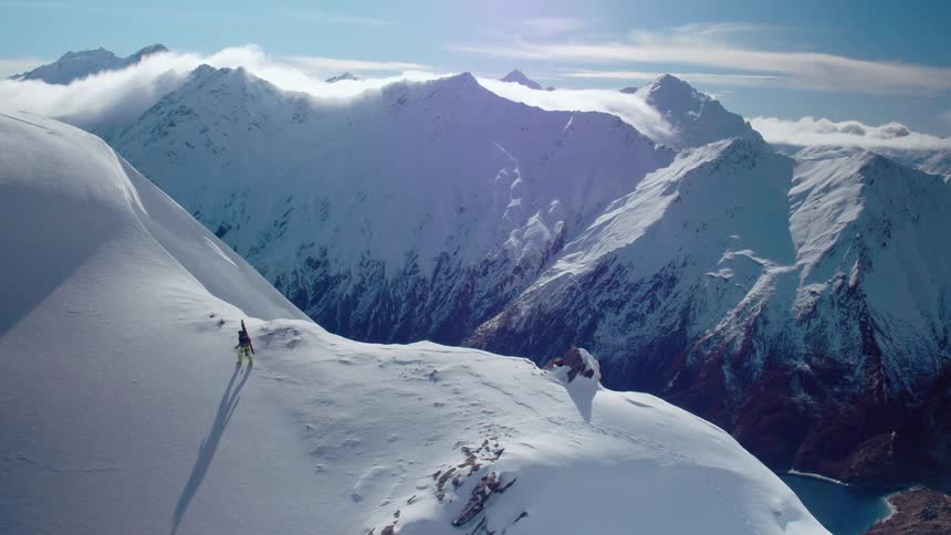A hiker hikes across the summit of a snow covered mountain under a clear daytime sky