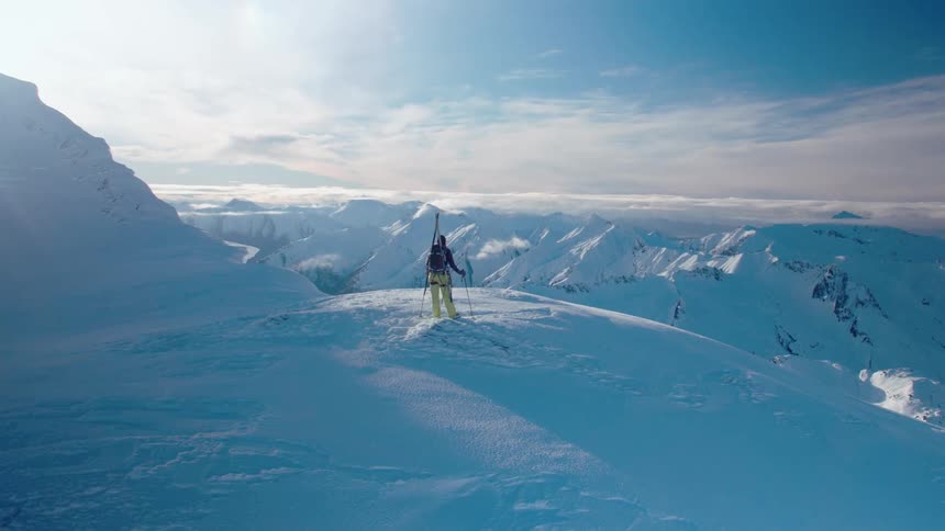 A mountaineer standing on the edge of a mountain looks out over the wintry landscape below