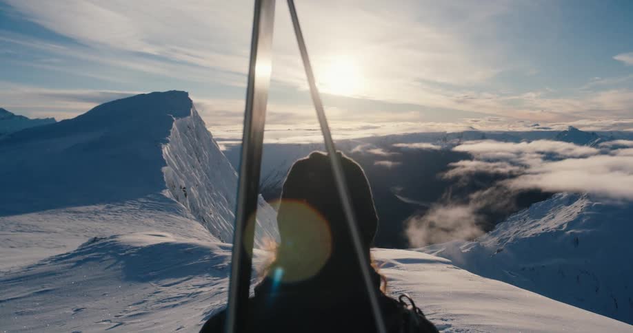 A skier stands at the top of a mountain and looks out at the landscape