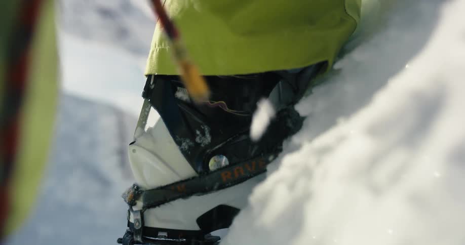 A person getting ready to climb a snowy mountain kicks their boot in to the snow