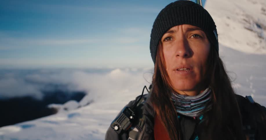 A female hiker hikes across a snow covered mountain on a sunny day