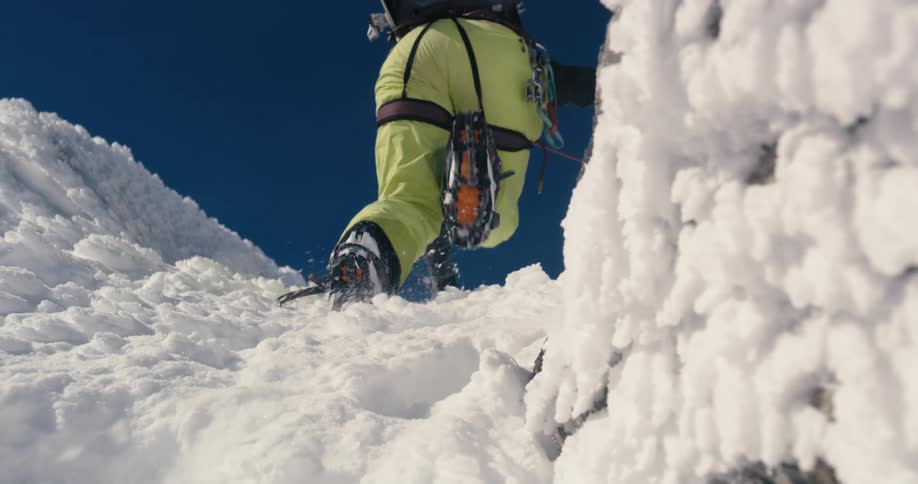 A hiker wears shoots with snow grips to climb up the side of a mountain