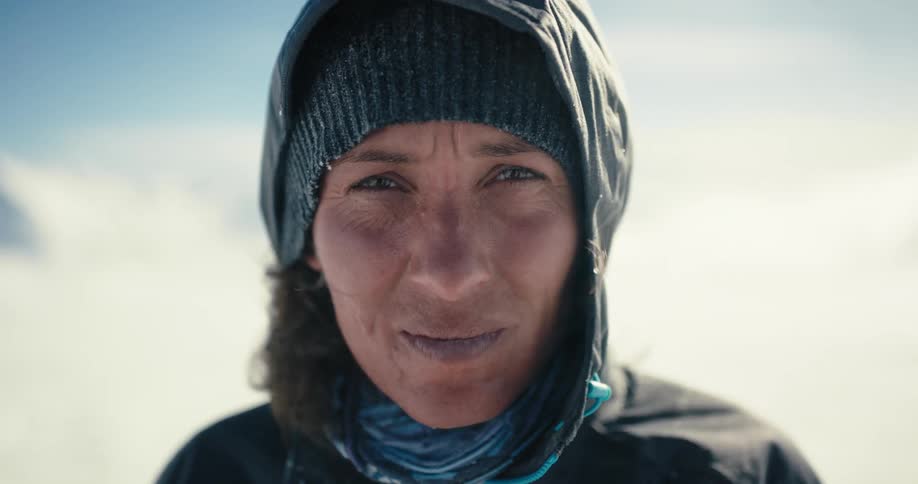 A woman standing outside turns and looks at the snow covered mountain behind her