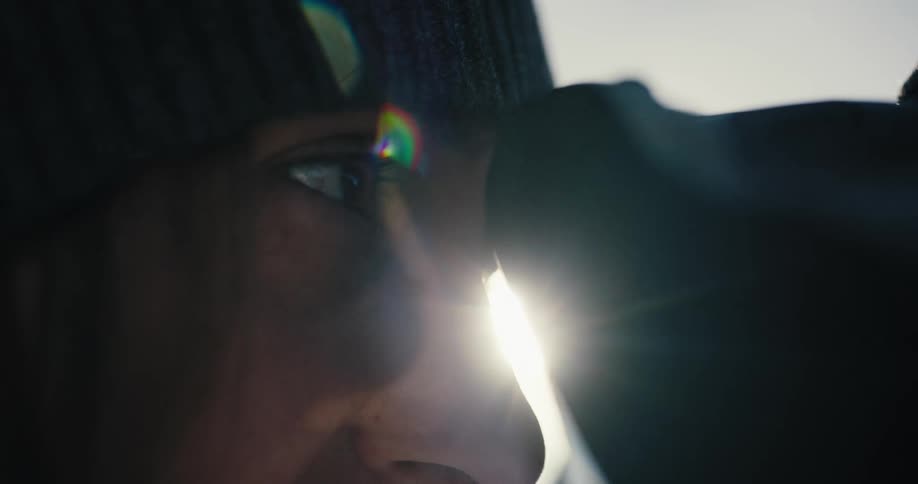 A woman with a hat looking through a camera with the sky and sun in the background