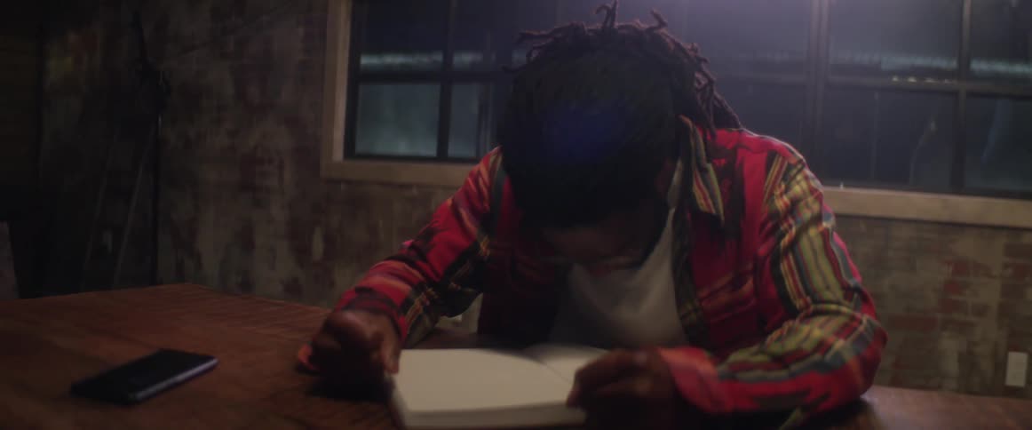 A man sits a table writing in a book then slams his fists down in anger
