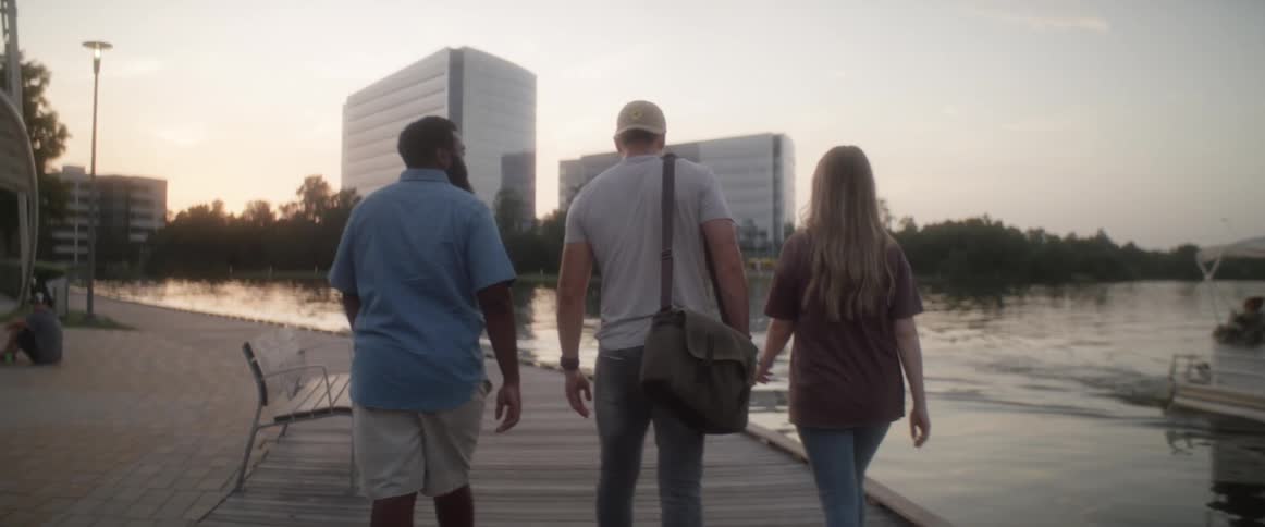 Two men and a woman walk along a river side boardwalk