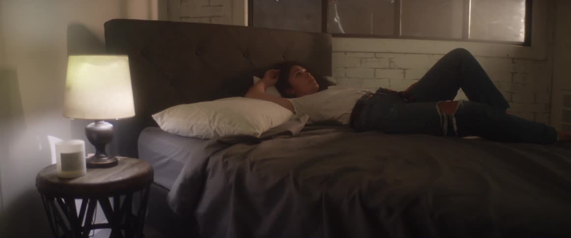 Woman with a white shirt and ripped jeans lies on bed in bedroom
