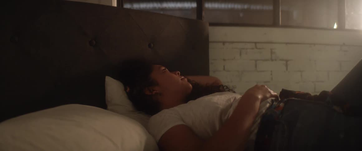 Woman with a white t shirt and ripped jeans lies on bed in dim lit bedroom