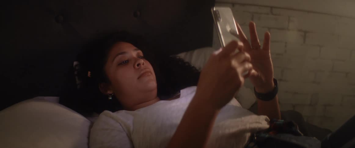 A teenage girl lying in bed scrolling on her cell phone