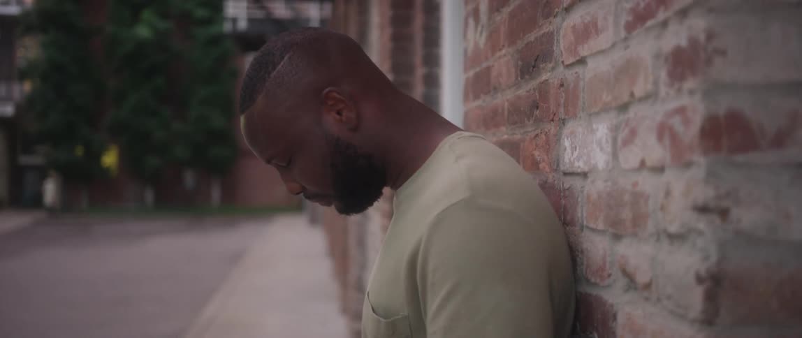 Young man holds hands in prayer reclined on a brick wall in the street
