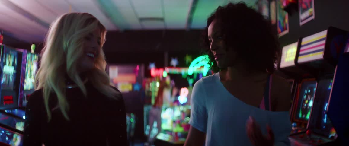 A pair of women talk while walking through a gaming arcade