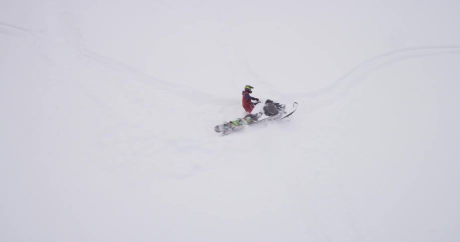 A snowmobile is driving and doing turns on a steep slope