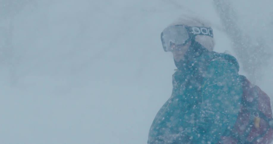 Person wearing cold weather gear and goggles stands in heavy snowfall
