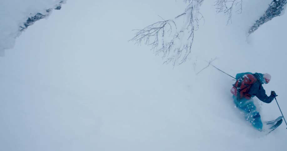 A skier travels through deep snow on a mountain slope as snow falls from the sky