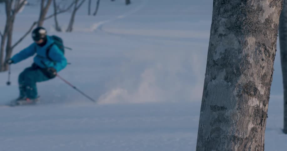 A skier in a blue coat gliding down a snowy mountainside in winter
