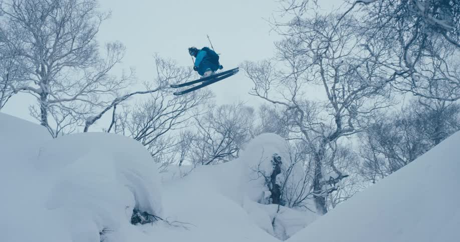 A skier spins off a cliff and falls in to the snow below