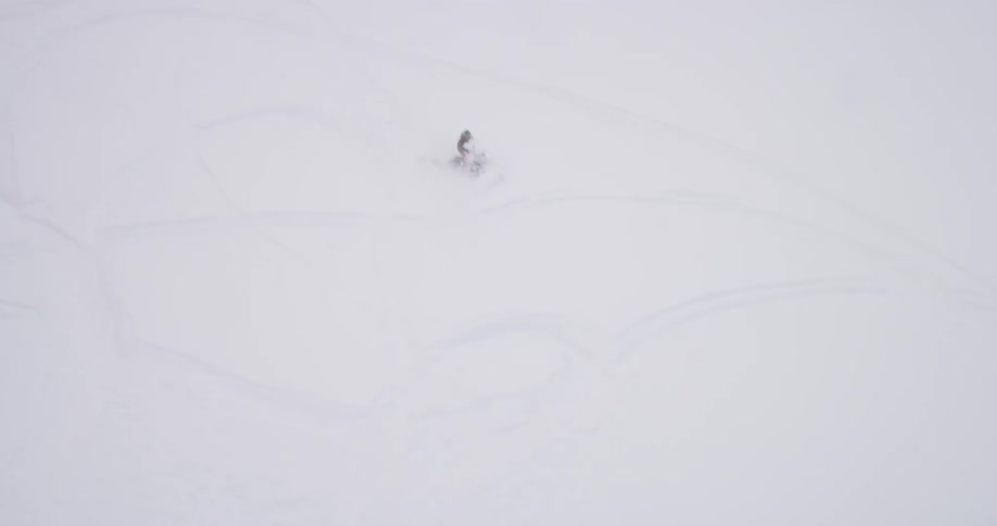 A person rides a snowmobile down a snow covered mountain