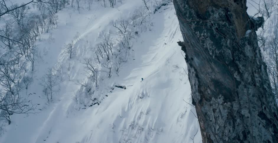 A skier descends a tall snow covered mountain slope during the day