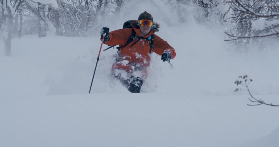 A skier in an orange coat speeding down a snowy mountainside in winter