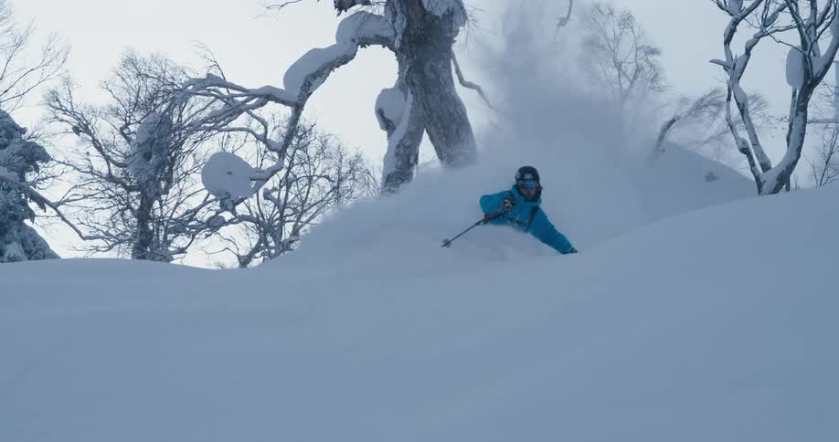 A skier flies into the air and does a pose before landing and continuing downhill