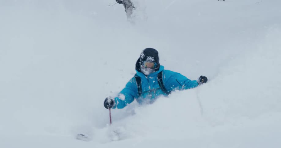 A skier kicks up snow as he navigates his way between trees on a mountain