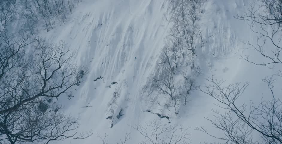 A skier descends a steep snow covered mountain slope during the day