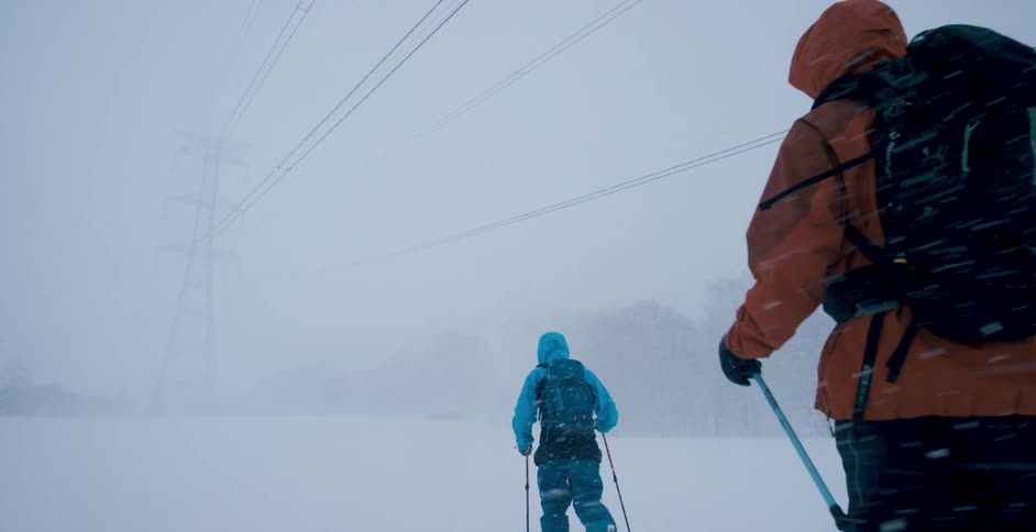 A pair of hikers hike through field covered in snow in a snowstorm during the day