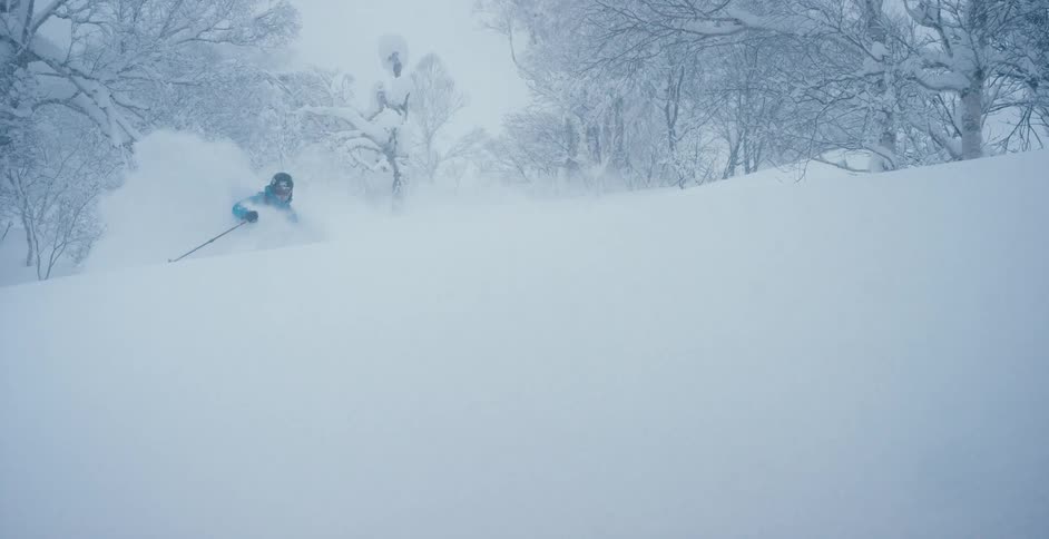 An athlete skis down a hill through deep white snow near the forest