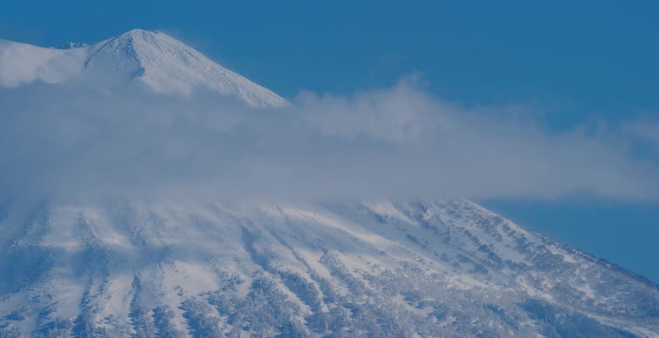 Clouds blowing in front of a mountain covered in snow