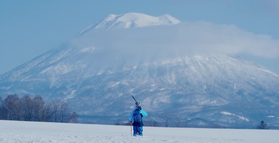 A skier standing at the bottom of a mountain looks up at it
