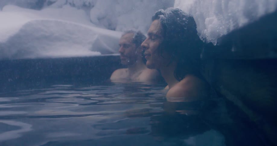 Two men are resting in the steamy water as it snows