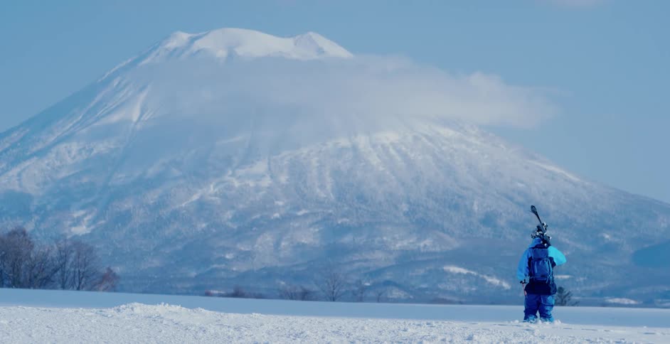 Skier wearing blue winter gear looks pensively at the snow covered mountain peaks