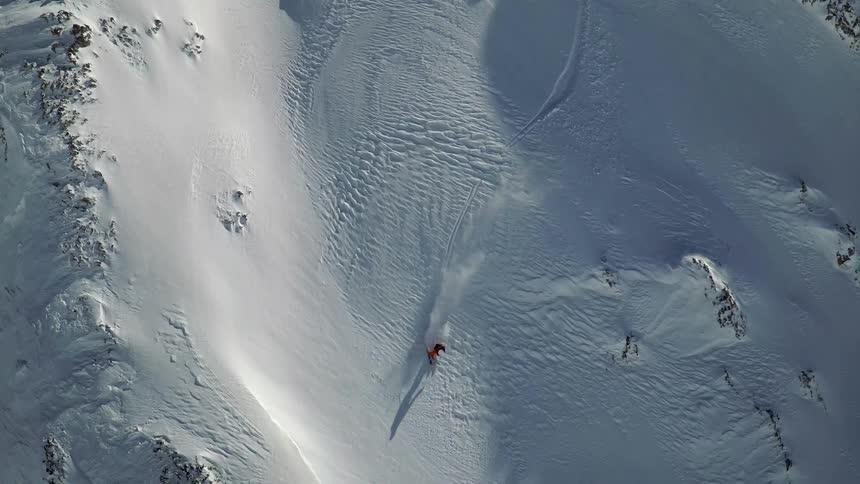 Skier skis down snow covered mountain slope kicking up snow as they ski in and out of shadows