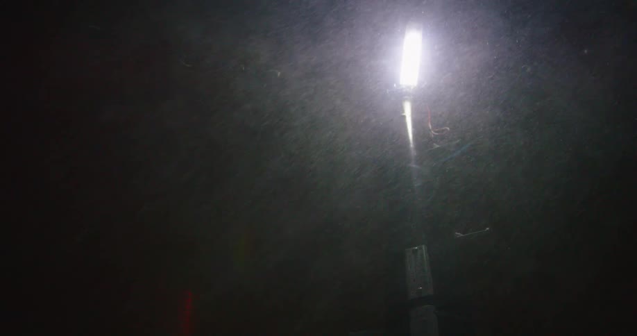 Snow falling around a street lamp during a blizzard at night