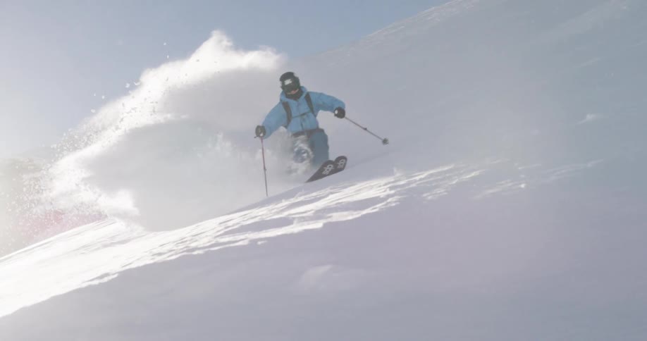 A skier in a blue coat speeding down a snowy mountainside on a winter day