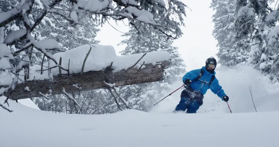 A skier in a blue coat gliding down a snowy mountainside in winter