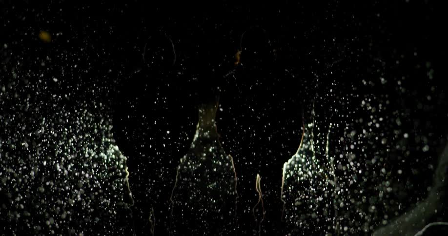 Three people walk with their hands in the pockets as heavy snow falls and a bright light shines on them