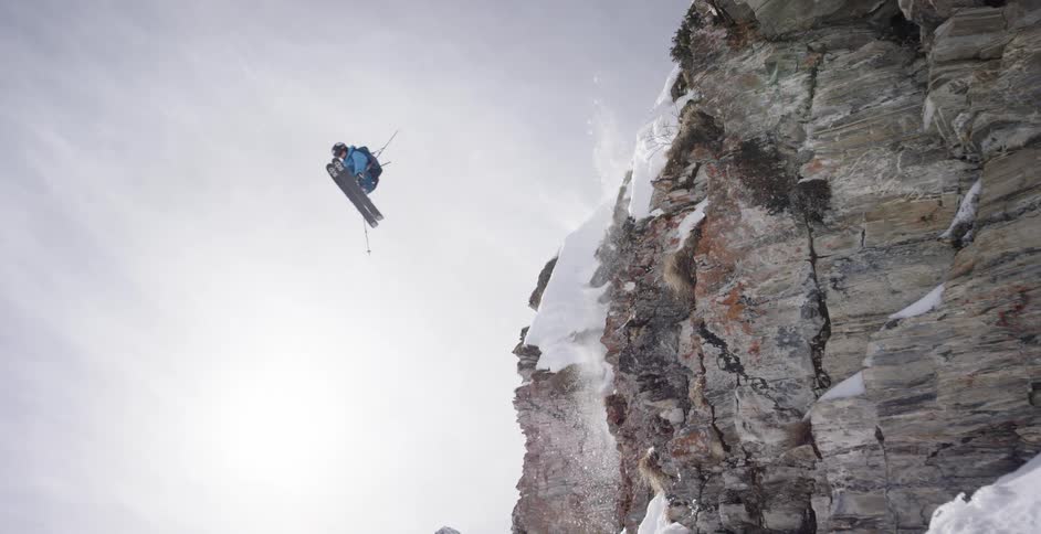 A skier jumps from off a tall cliff and onto a snow covered slope